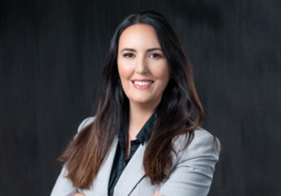 A female personal injury accident lawyer in a grey jacket against a black background who can help clients understand when to hire a personal injury lawyer