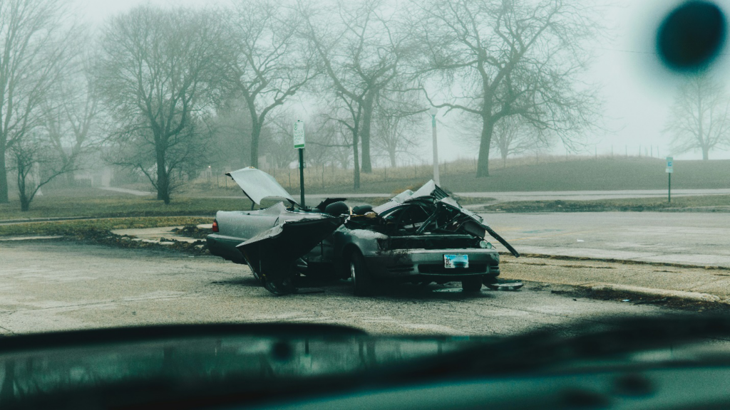 A grey car totally wrecked against the background of a misty landscape with bare trees, showing why victims of personal injury and car crashes must approach personal injury and car accident lawyers for compensation.