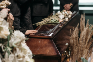A bunch of flowers lies on top of a closed casket as someone places their hand on it, showing how compassionate legal support for wrongful death can help those grieving a loss.
