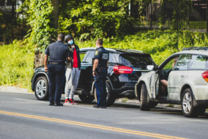 Two police officers stand in front of a person in a red shirt and gray sweatpants