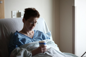 A person with short hair and glasses, lying in a hospital bed