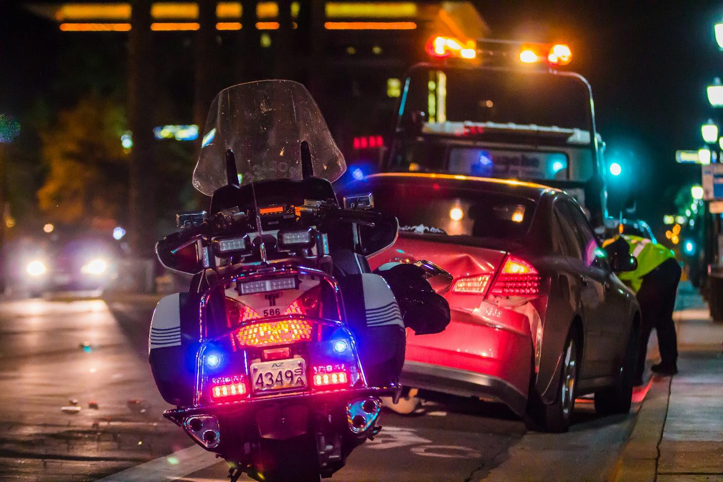 A police motorcycle stands guard as a tow truck prepares to haul away a damaged car