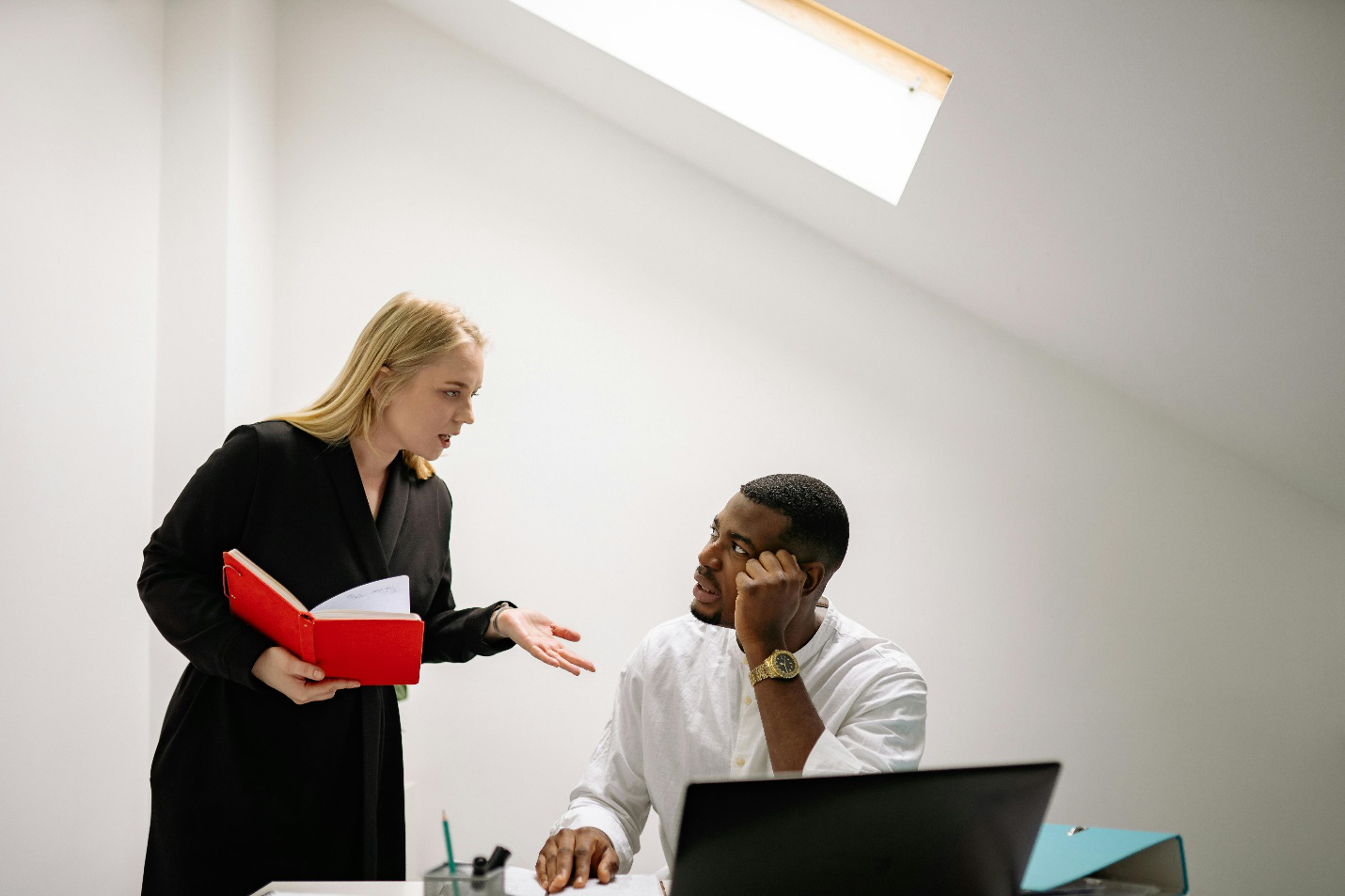 a woman talking to a man while he is sitting at his desk