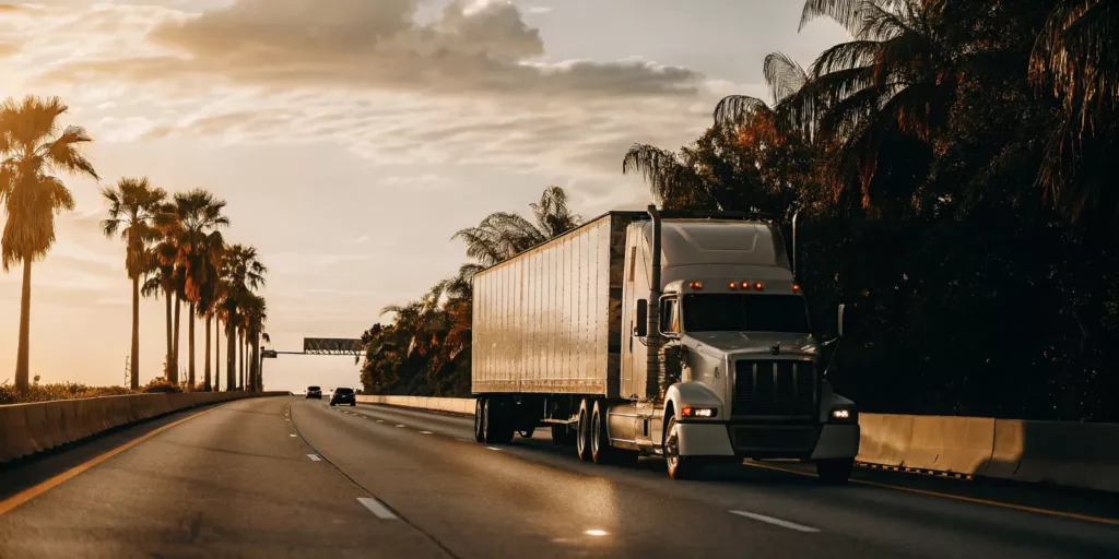 Semi-trailer truck driving on a Florida highway at sunset with palm trees in the distance
